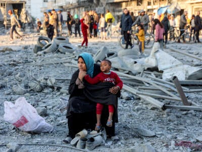 A woman sits with a child and salvaged footwear amid debris and rubble at the site of Israeli bombardment on a residential block in Jalaa Street in Gaza City on January 14, 2025.