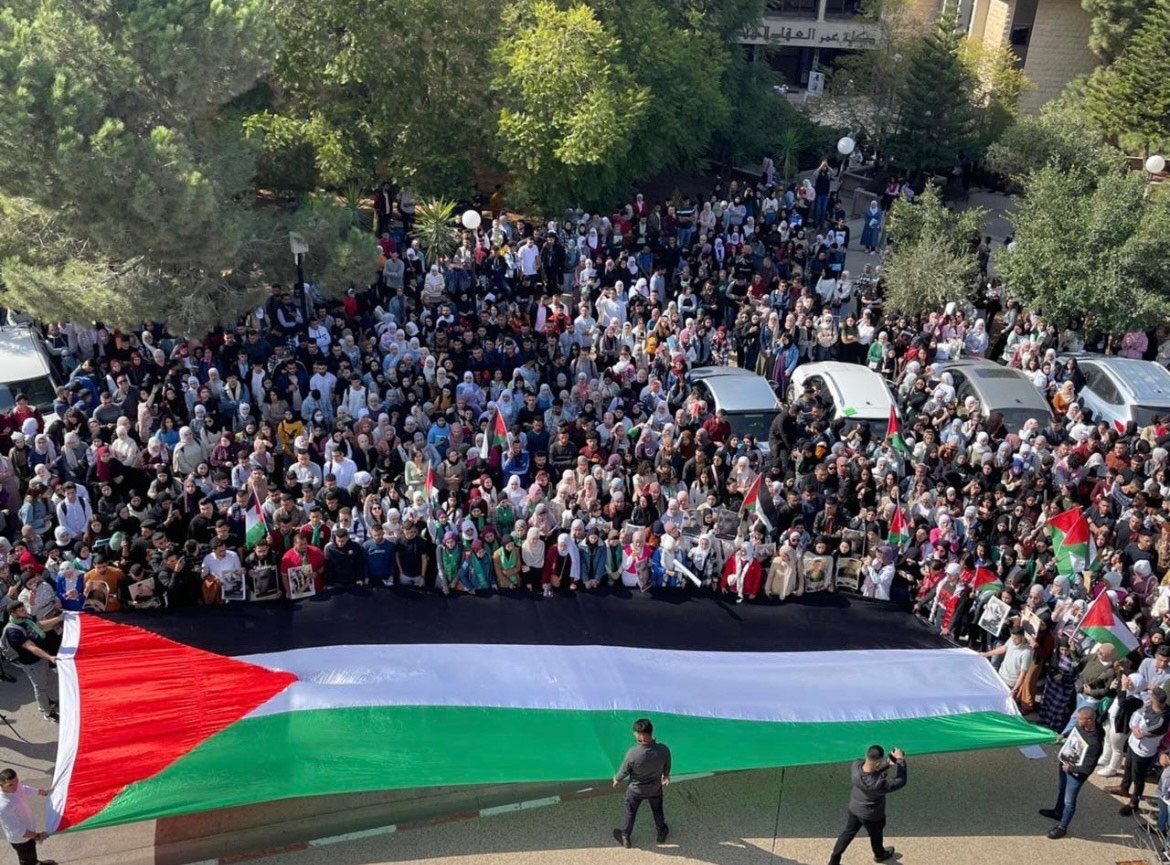 In front of the Palestinian flag, students protest Israeli crimes committed under occupation.