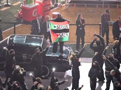 A protestor holds a Palestinian flag with the words "Gaza" and "Sudan" as US rapper Kendrick Lamar performs during Super Bowl LIX Chiefs vs Eagles Apple Music Halftime Show at Caesars Superdome in New Orleans, Louisiana, February 9, 2025.