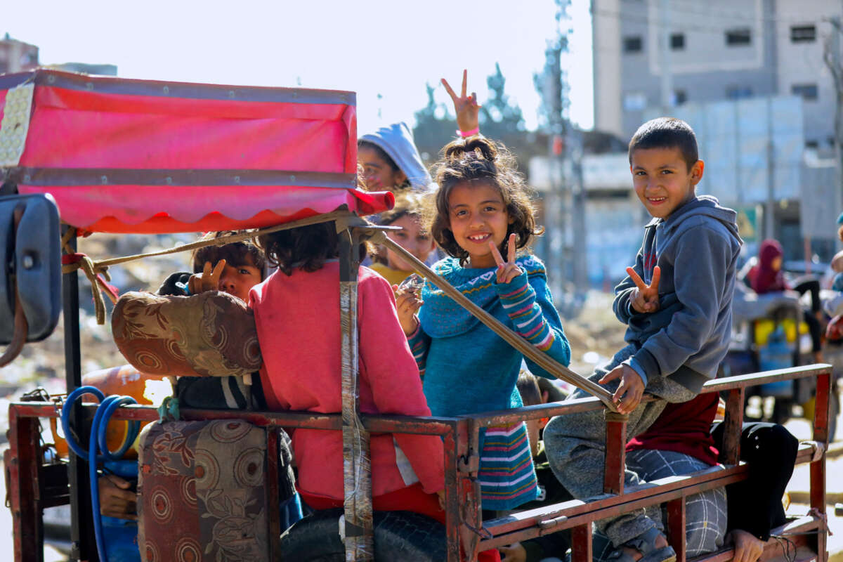 Palestinian children throw up peace signs and smile while in the back of a truck