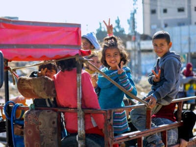 Palestinian children throw up peace signs and smile while in the back of a truck