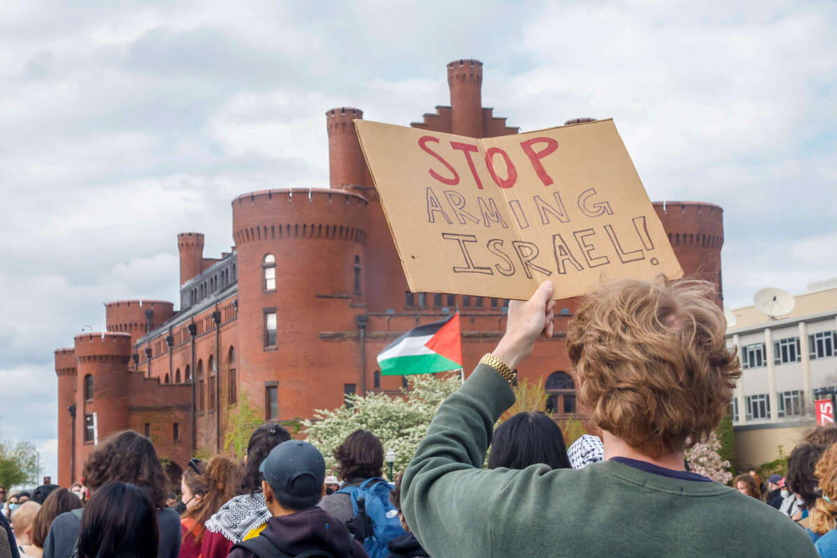 A protester holds a cardbord sign reading "STOP ARMING ISRAEL" during an outdoor demonstration