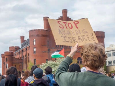 A protester holds a cardbord sign reading "STOP ARMING ISRAEL" during an outdoor demonstration