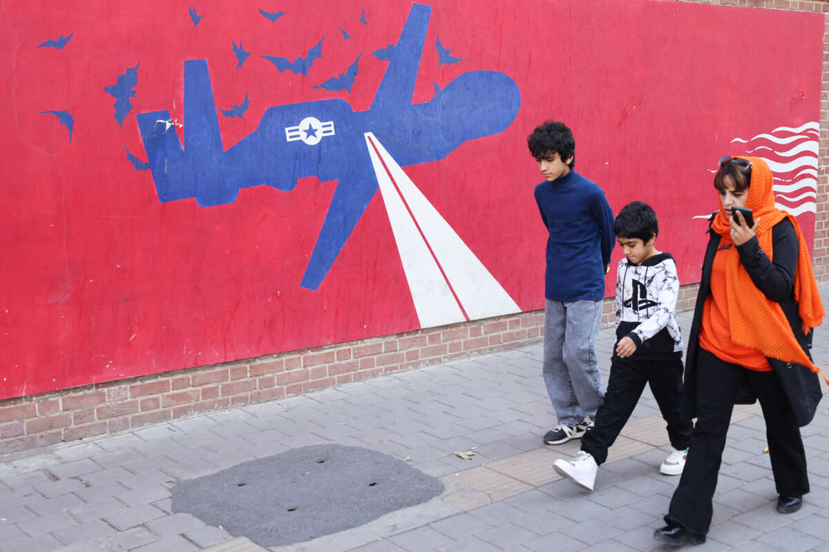 Children and their mother walk by a mural depicting a us military drone surrounded by bats