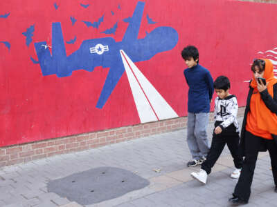 Children and their mother walk by a mural depicting a us military drone surrounded by bats