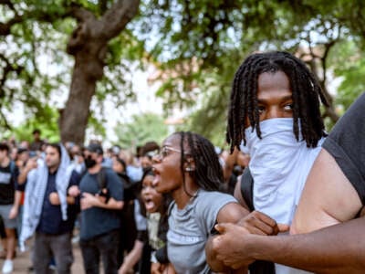 Students of color link arms and chant during an outdoor protest