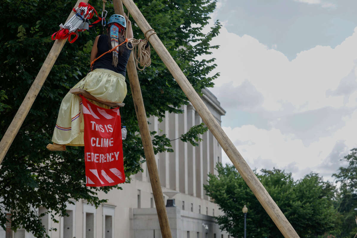 Activists with Ikiya Collective hang from a structure as they close a road in front of the Department of Interior