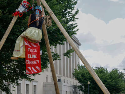 Activists with Ikiya Collective hang from a structure as they close a road in front of the Department of Interior