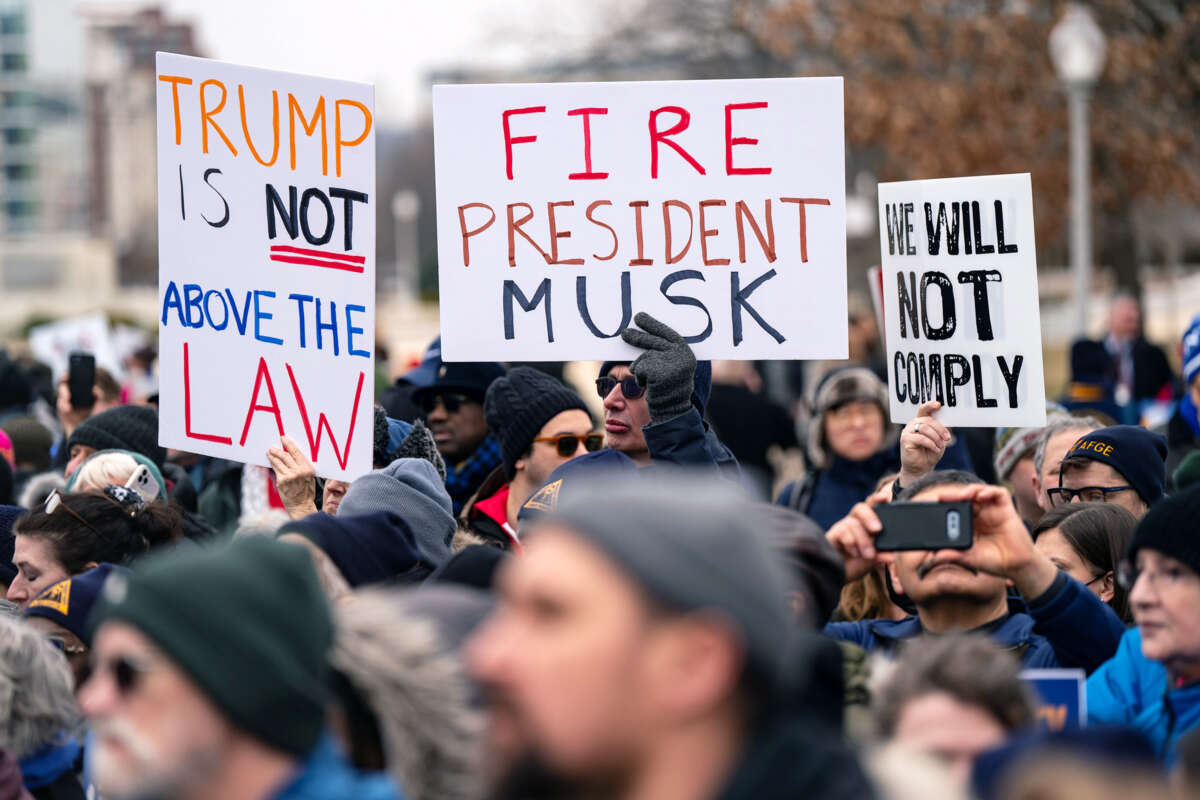 A protester holds a sign reading "FIRE PRESIDENT MUSK" during an outdoor demonstration