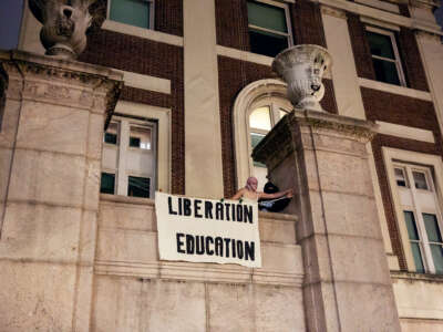 Two students unfurl a banner reading "LIBERATION; EDUCATION" at a university building