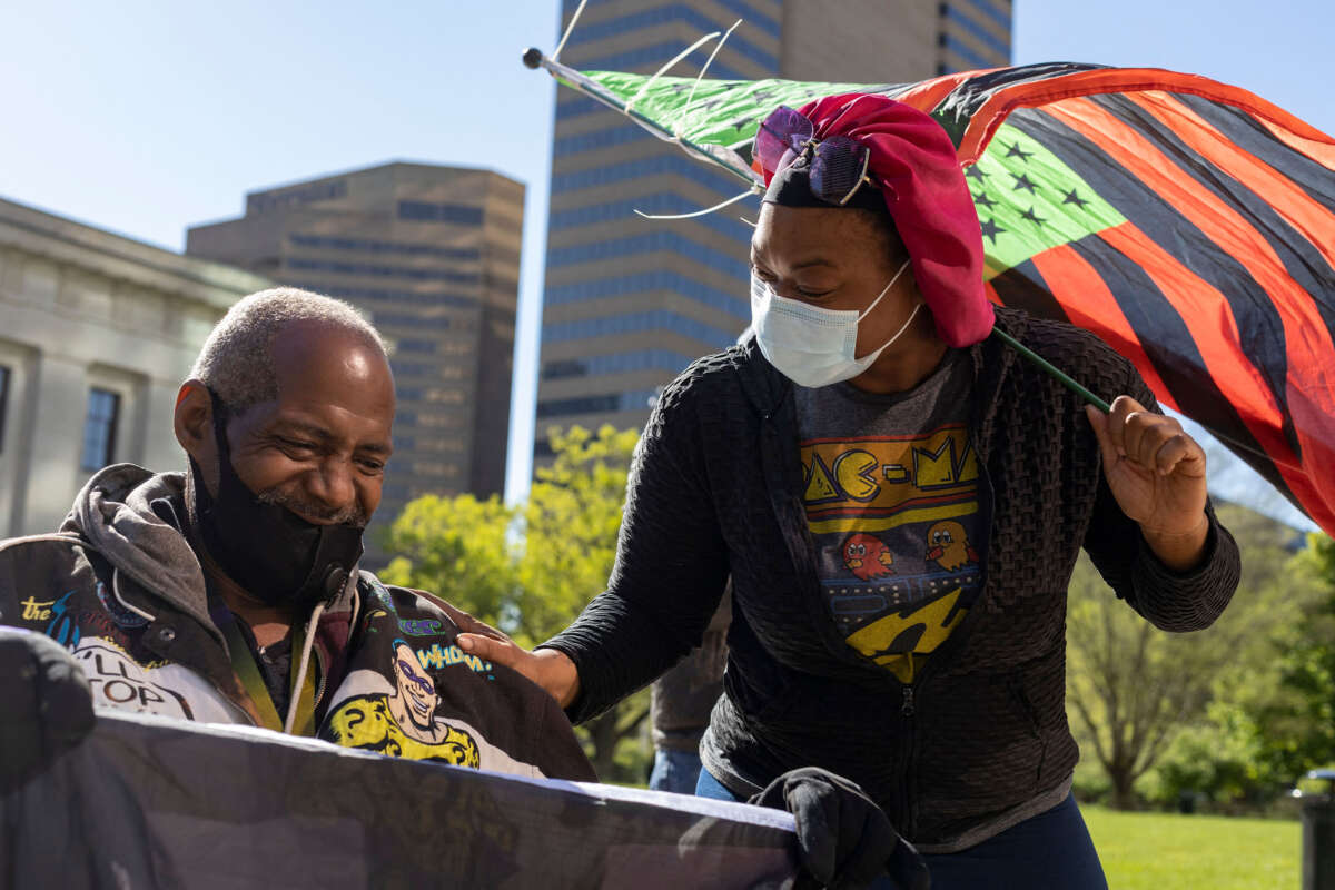 A Black Lives Matter (BLM) activist holds a BLM flag in his wheelchair alongside another activist connecting with him while holding an Afro-American flag in front of the Ohio Statehouse during a protest against police brutality in Columbus, Ohio, on May 1, 2021.