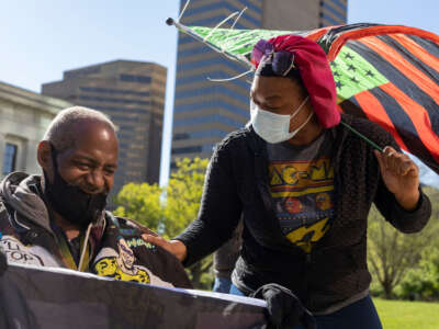 A Black Lives Matter (BLM) activist holds a BLM flag in his wheelchair alongside another activist connecting with him while holding an Afro-American flag in front of the Ohio Statehouse during a protest against police brutality in Columbus, Ohio, on May 1, 2021.