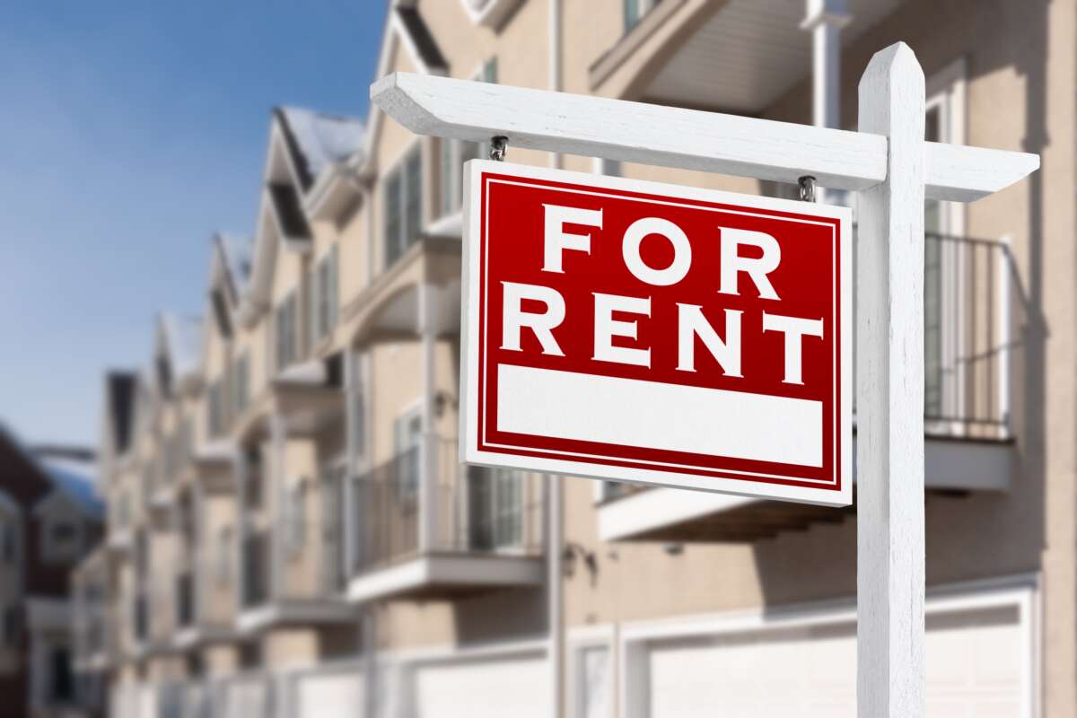 “For Rent” sign in front of a row of apartments.