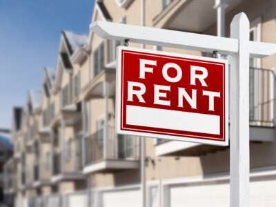 “For Rent” sign in front of a row of apartments.