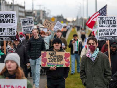 Protesters hold signs during a march against Immigration and Customs Enforcement (ICE) entitled "Get our Gente Out of Guantanamo Bay!" in Seattle, Washington, on February 8, 2025.