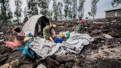 An elderly woman and her two daughters-in-law stand in front of one of the last remaining shelters in the Bulengo internally displaced persons camp after it was burned down, in Bulengo, Democratic Republic of Congo, on February 17, 2025.