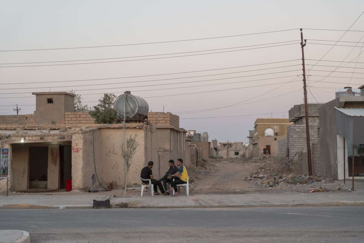 People sit among the partly destroyed buildings of a village in northern Sinjar, where Yazidi have recently begun to return.