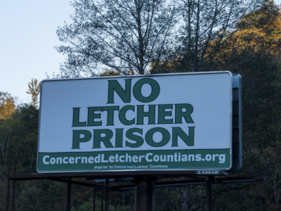 A billboard reads "No Letcher Prison, ConcernedLetcherCountians.org, Paid for by Concerned Letcher Countian," in opposition to a proposal for a Federal Prison in Letcher County, Kentucky.