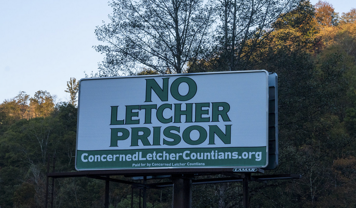 A billboard reads "No Letcher Prison, ConcernedLetcherCountians.org, Paid for by Concerned Letcher Countian," in opposition to a proposal for a Federal Prison in Letcher County, Kentucky.