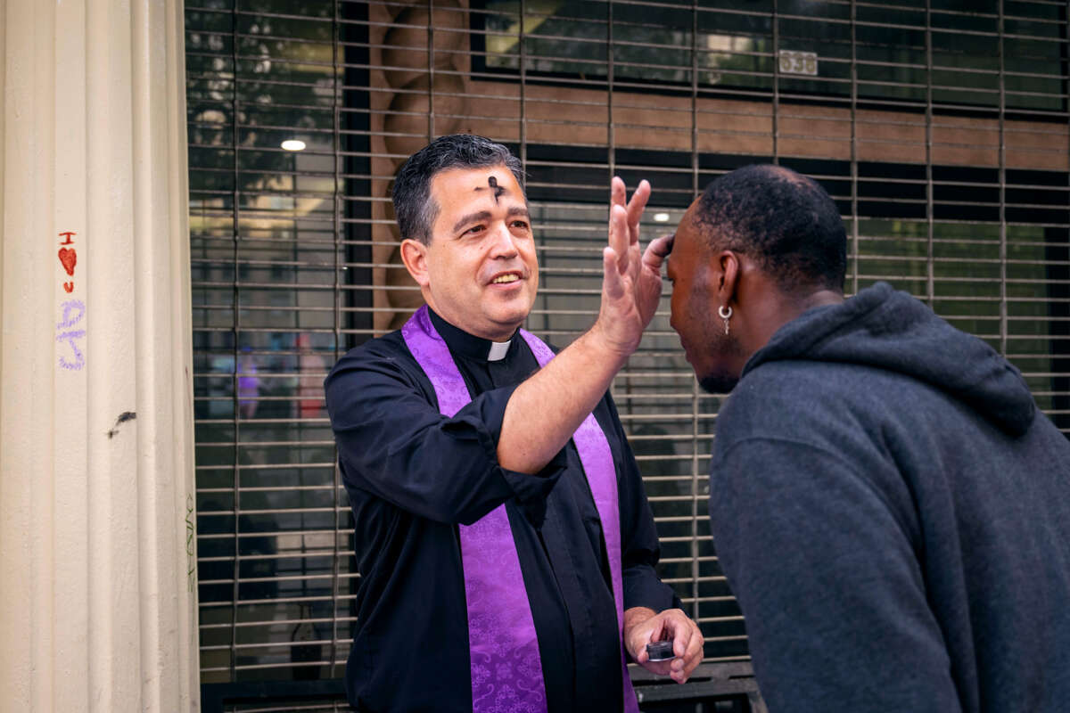 A priest with an ashen cross on his forehead anoints a man's brow