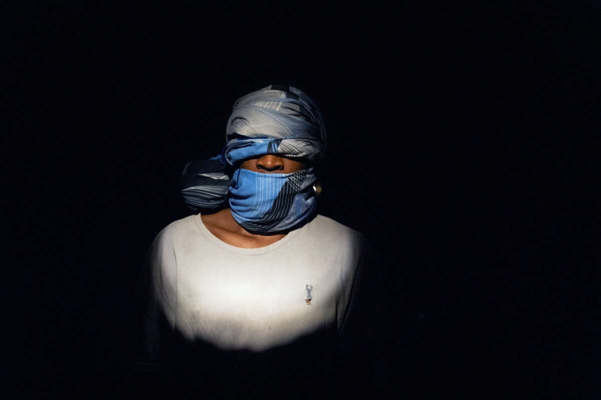 A gagged and blindfolded man stands in complete darkness