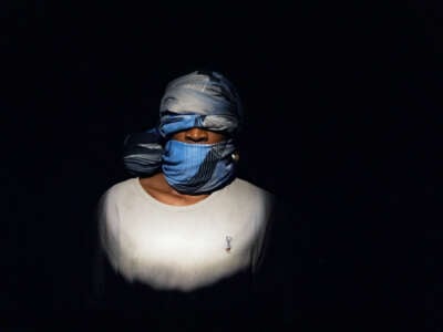 A gagged and blindfolded man stands in complete darkness