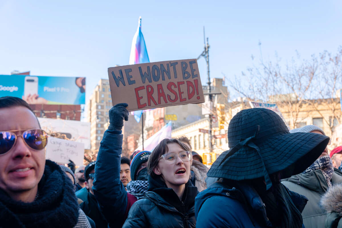 A person holding a sign reading "WE WON'T BE ERASED" participates in an outdoor protest