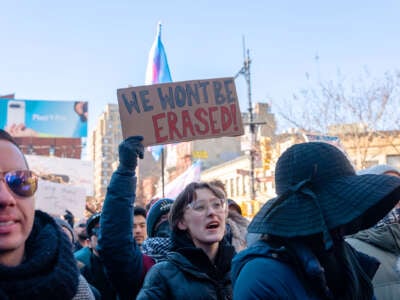 A person holding a sign reading "WE WON'T BE ERASED" participates in an outdoor protest