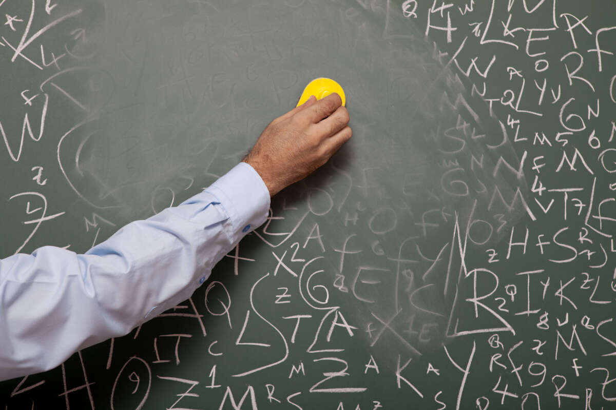 Human hand erasing blackboard with large amount of letters written on.