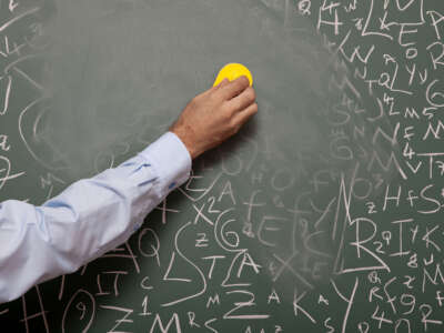 Human hand erasing blackboard with large amount of letters written on.