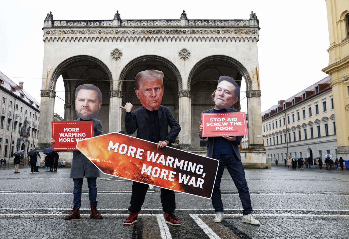 Three protesters dressed up as JD Vance, Donald Trump (holding a sign reading "MORE WARMING, MORE WAR" and Elon Musk pose for a photo