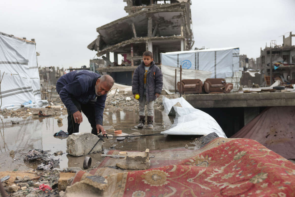 A Palestinian boy watches as a displaced man sets up a tent on a rainy day amid destroyed buildings in Jabalia in the northern Gaza Strip on February 6, 2025, during a truce in the war between Israel and Hamas.