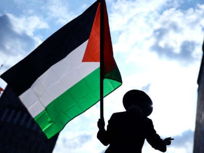 A protester in a broad-rimmed hat waves a Palestinian flag