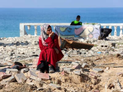 A woman sits by rubble as she waits along Gaza's coastal al-Rashid Street for people to cross from the Israeli-blocked Netzarim corridor from the southern Gaza Strip into Gaza City on January 26, 2025.