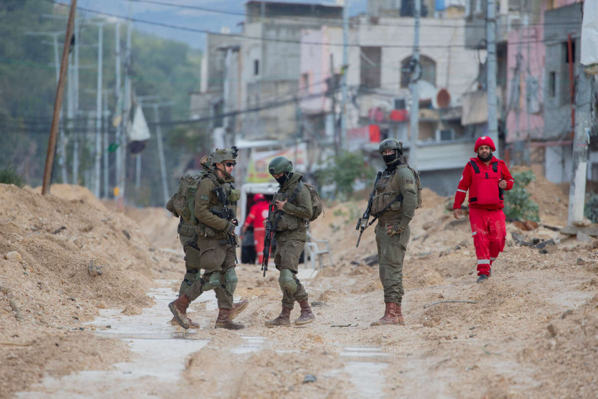 Israeli soldiers walk along a muddy street as a humanitarian worker walks by in Nur Shams refugee camp in the West Bank, Palestine, on February 10, 2025.