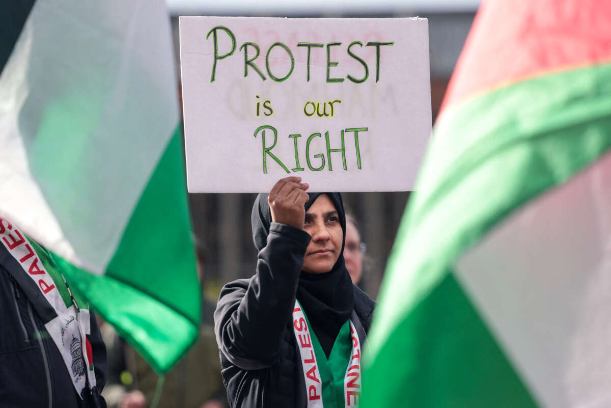 A woman in a black hijab holds a sign reading "PROTEST IS OUR RIGHT" during an outdoor protest in support of detained Mahmoud Khalil