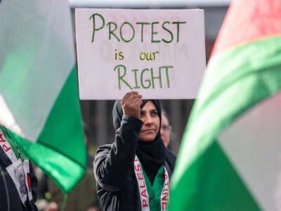 A woman in a black hijab holds a sign reading "PROTEST IS OUR RIGHT" during an outdoor protest in support of detained Mahmoud Khalil