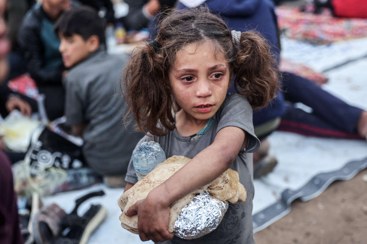 A little girl with a tear-streaked face clutches pita and food wrapped in foil