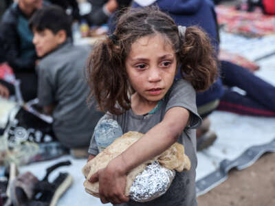 A little girl with a tear-streaked face clutches pita and food wrapped in foil