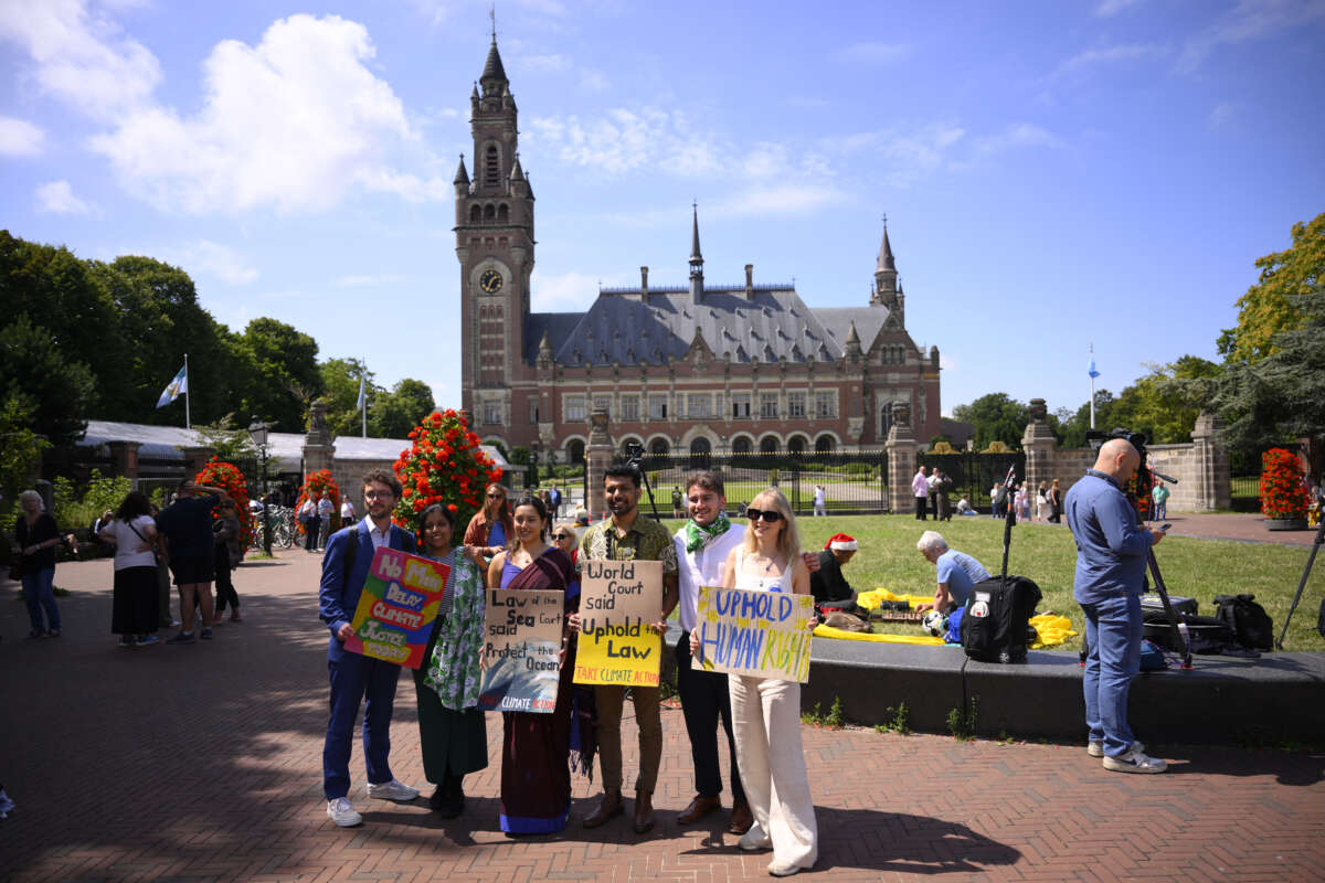 Joie Chowdhury, attorney for the Center for International Environmental Law; Vishal Prasad, director of Pacific Islands Students Fighting Climate Change; and Jule Schnakenberg, CEO of World's Youth for Climate Justice pose with signs ahead of the International Court of Justice session tasked with issuing the first Advisory Opinion on States' legal obligations to address climate change, in The Hague, on July 23, 2025.