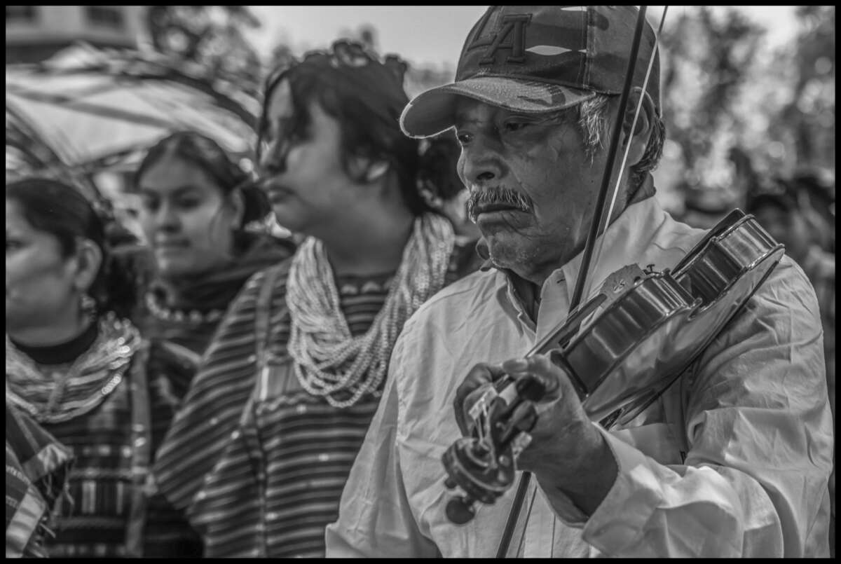 Un violinista toca la música que acompaña a las bailarinas de triqui detrás de él.