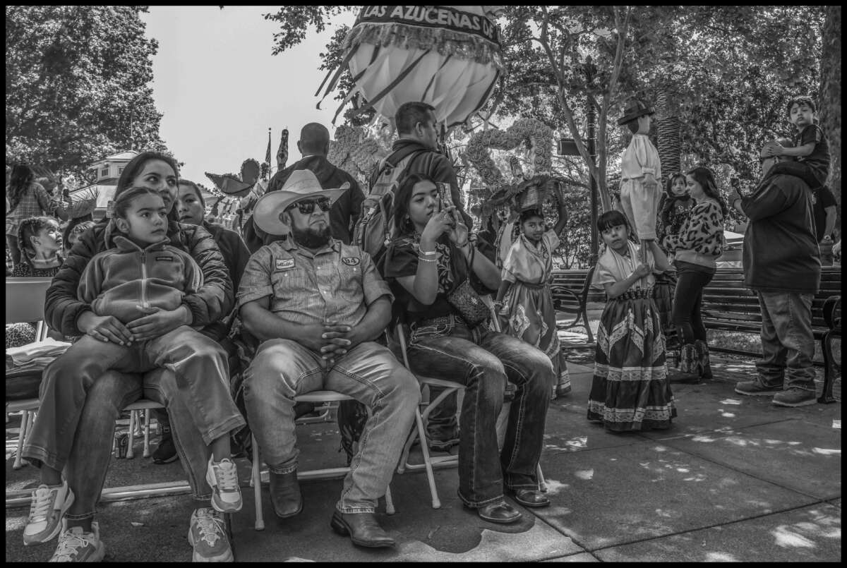 Una familia en la plaza observa la Calenda, junto con dos jóvenes artistas de Las Azucenas de María.