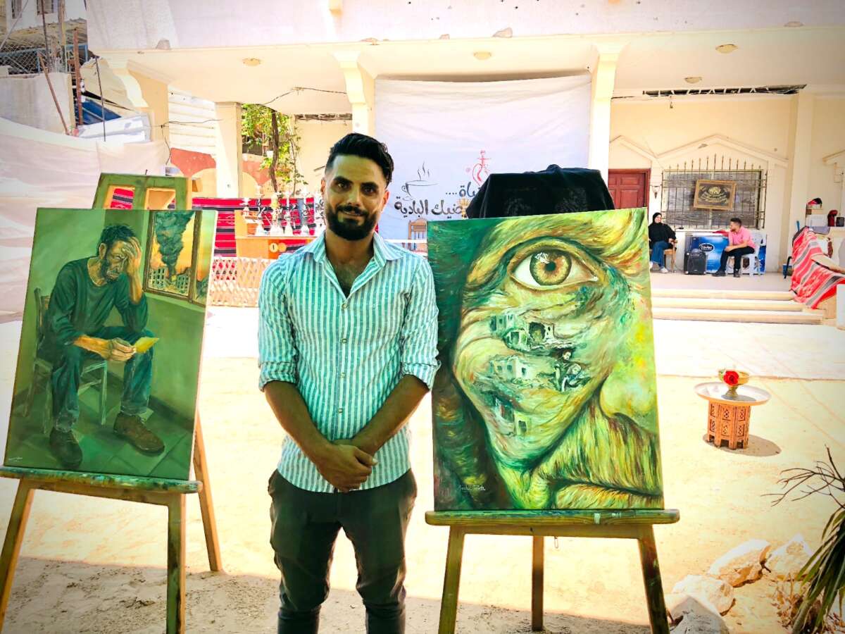 Fadal Tafish se encuentra junto a su obra de arte, titulada Feature of a Homeland, que representa el hecho de una mujer mayor con edificios colocados sobre la parte superior.