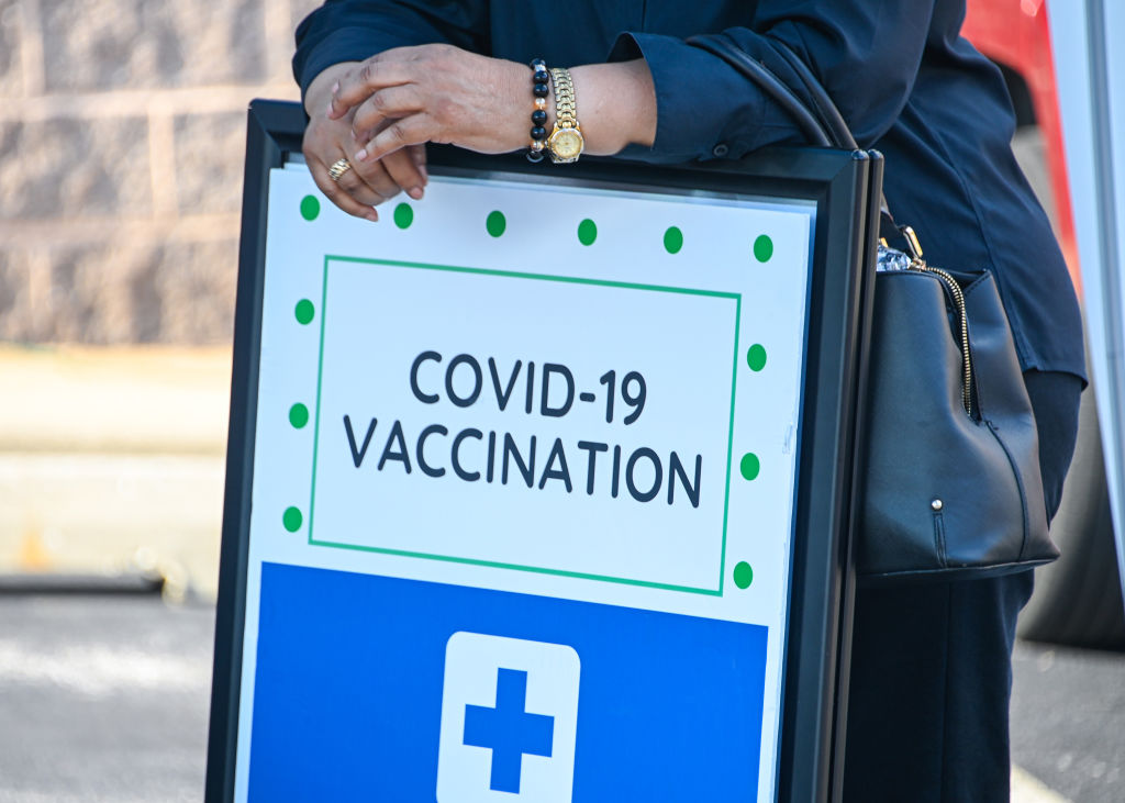 A woman leans on a COVID-19 vaccine registration sign at a back-to-school vaccine fair