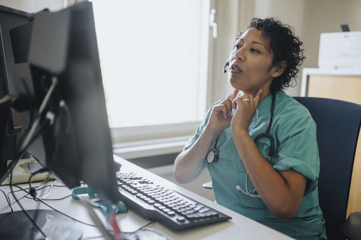 A doctor gives advice through a video call while sitting at a desk in a hospital.
