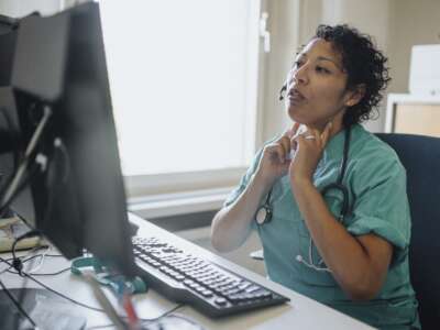A doctor gives advice through a video call while sitting at a desk in a hospital.