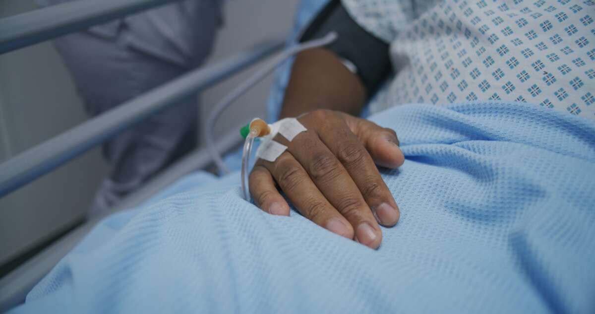 A patient lies on a gurney with a venous catheter in their hand.