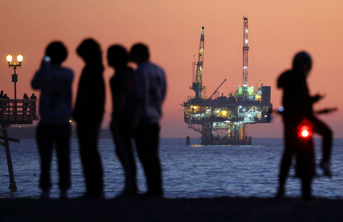 People gather at the beach after sunset with an offshore oil and gas platform in the distance on January 5, 2025, in Seal Beach, California.