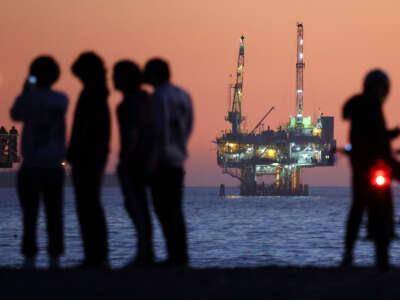 People gather at the beach after sunset with an offshore oil and gas platform in the distance on January 5, 2025, in Seal Beach, California.