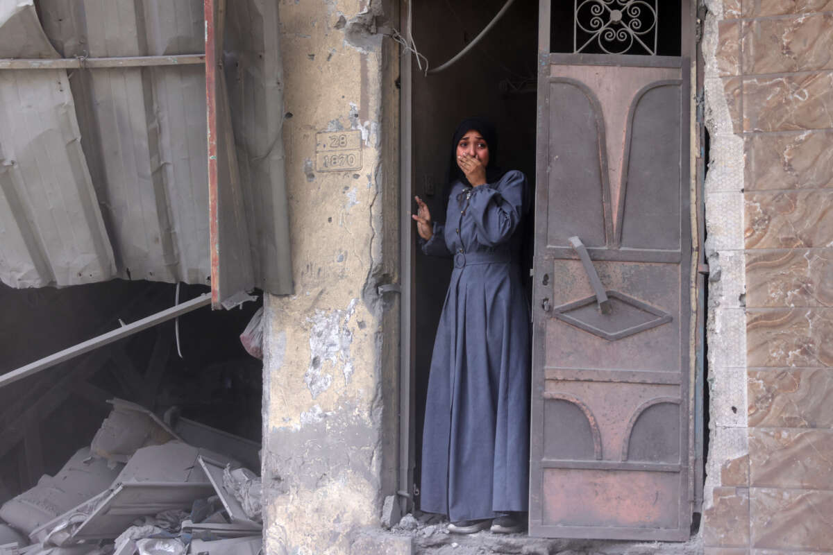 A Palestinian woman standing in a doorway observes the aftermath of an Israeli strike that hit Gaza City's southern Al-Zaytoun neighborhood on August 8, 2025.